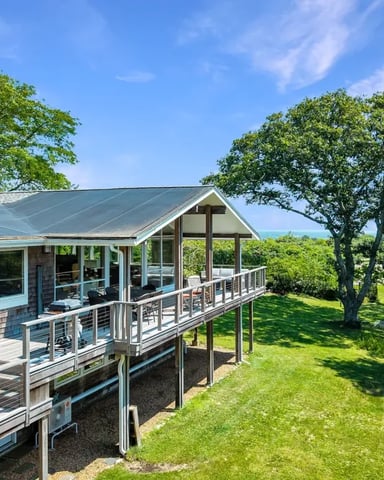Modern cottage with metal roof and wraparound deck overlooking grassy lawn and mature trees