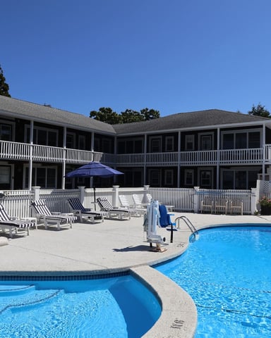 Large residential building with white railings and multiple pools in foreground, lounge chairs and blue umbrella on patio deck
