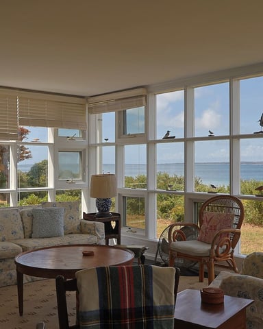 Sunroom with upholstered seating, round table, and expansive windows overlooking ocean and coastal landscape