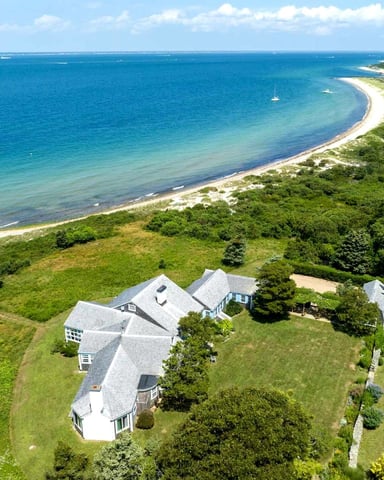 Aerial view of waterfront homes on green lawn overlooking curved sandy beach and turquoise ocean