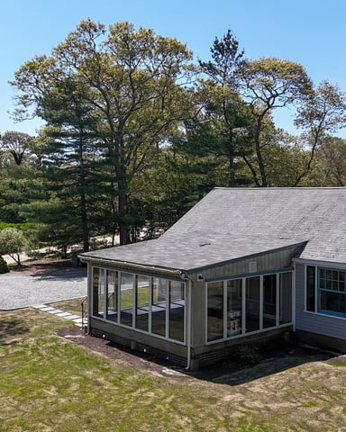 A blue house perched on a grassy bluff above a sandy beach, with white-capped ocean waves below